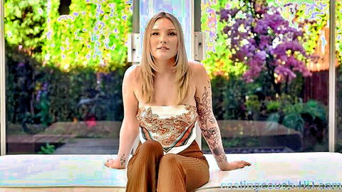 Seductive tattooed blonde woman sitting smiling in crop top and pants