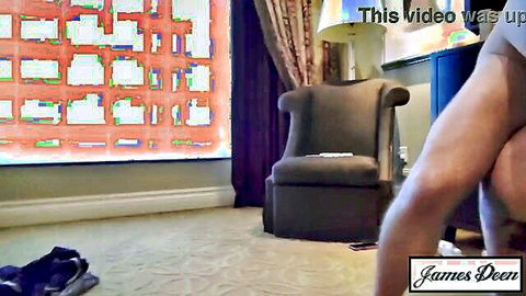 Naked man standing with pants down exposing bare ass near armchair in luxury hotel room