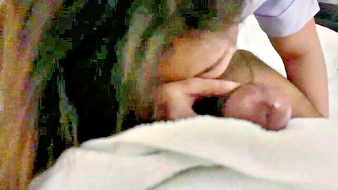 Thai nurse leaning over patient with exposed newborn baby in bed