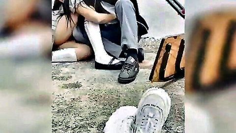 Asian schoolgirl in uniform sits intimately with guy in casual clothes, friend filming nearby