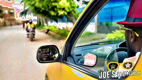Stylish ebony man with yellow shades and red hat driving yellow taxi on outdoor street
