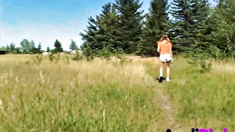 Blonde Andi Pink in orange top and white shorts walking in sunny woods
