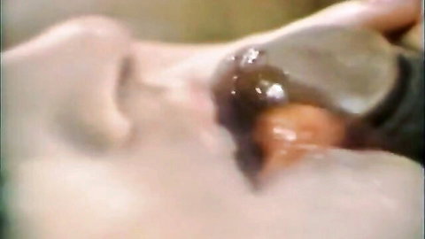 Close-up of woman performing oral on toy in kinky couples scene with tongues and play