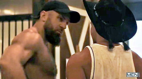 Two burly muscular men in hats facing off shirtless in intense gay encounter