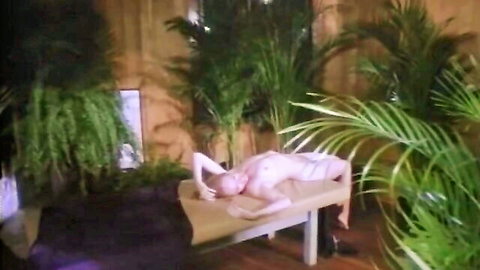 Nude curvy woman arches back on massage table exposing bare ass and pussy in tropical plant room
