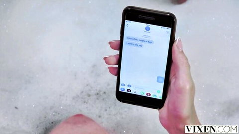 Woman's hand holds phone in steamy bubble bath displaying I love you text message