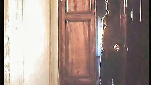 Shadowy figure lurking behind half-open wooden door in dimly lit vintage room