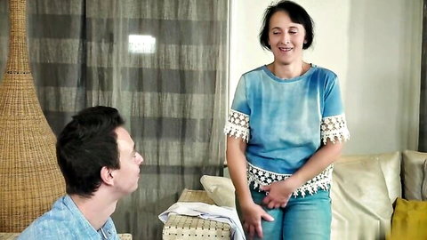 Mature brunette MILF in tight jeans grabs crotch smiling down at kneeling young man