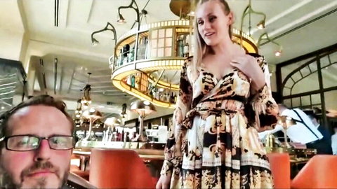 Blonde babe in revealing gold dress flaunting deep cleavage in luxury bar with bearded man