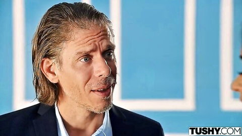 Long-haired handsome man in dark suit speaking on blue studio background