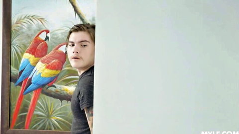 Young man in black shirt posing beside vibrant red and blue parrot painting