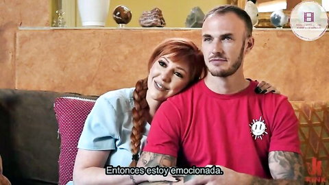 Excited redhead babe cuddles tattooed bald guy on couch smiling intimately