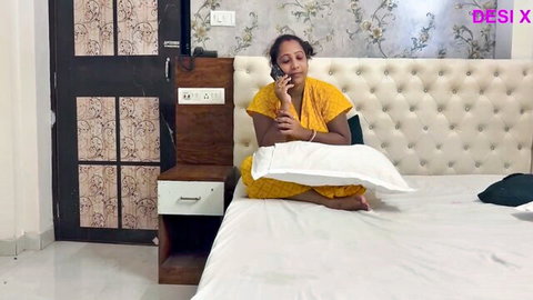 Sexy Desi Bhabhi in yellow outfit sits on bed talking on phone, teasing viewers