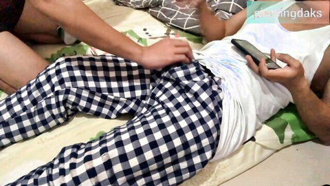 Pinay hand stroking Asian guy's cock bulge inside checkered pants while he holds phone