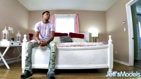 Handsome black stud in purple shirt and ripped jeans sitting on white bed