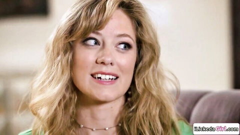 Smiling blonde woman with long wavy hair looking playfully at camera on couch