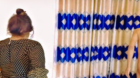 South Asian woman in sheer black top stands teasingly by curtains with muscular man's arm visible