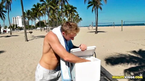 Muscular tanned hunk in tight white shorts bends over cooler on sunny beach teasing bulge