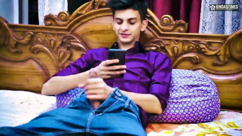 Young Indian man masturbating on bed while holding phone