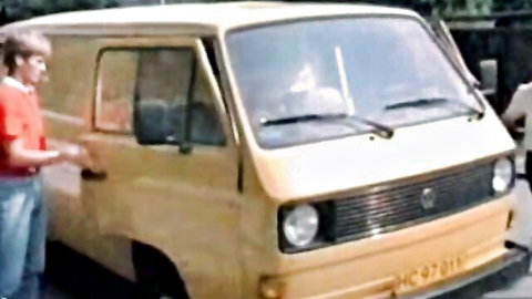 Two men in casual clothes stand by a yellow vintage VW van opening the door outdoors
