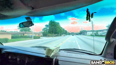 Stack of cash on car dashboard during road drive with colorful sky and Bang Bros watermark