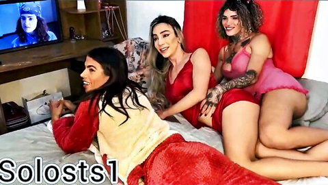 Three curvy Latinas in red and pink lingerie smiling playfully on bed at Prezotte's house