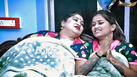 Indian stepmom and stepdaughter cuddling on bed in colorful outfits, taboo family tease
