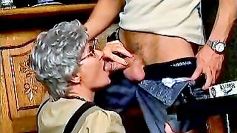 Mature gray-haired woman kissing young stud's abs in steamy foreplay