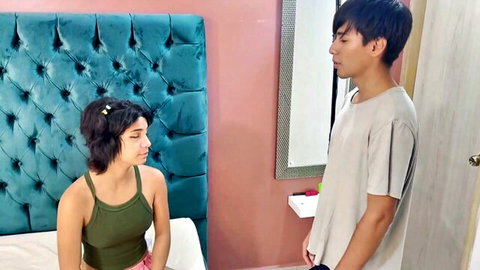 Naughty short-haired girl in green tank top stares seductively at stepbrother standing close by bed