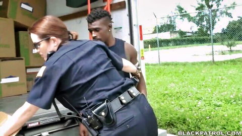 Redhead policewoman in uniform handcuffing muscular black suspect outdoors in warehouse lot