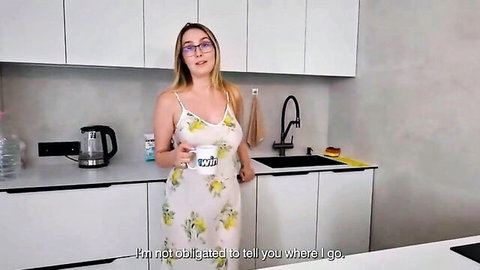 Blonde stepmom in tight floral dress holds mug smiling teasingly in kitchen