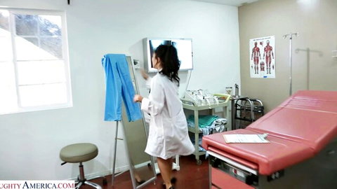 Sexy Asian MILF doctor in white lab coat standing by exam table in clinic