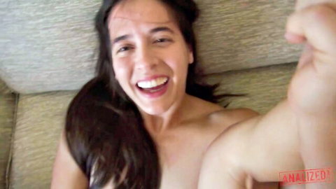 Skinny young brunette with small tits smiling topless in amateur couch selfie