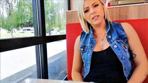 Blonde woman in denim vest smirks seductively at camera in diner booth POV