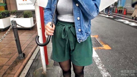 Japanese woman in denim jacket, green shorts, stockings, holding umbrella outdoors tease