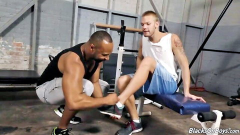 Muscular black trainer touching white student's ankle in gym workout