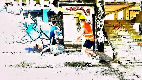 Two young men in hard hats and shorts kick soccer ball in graffiti alley