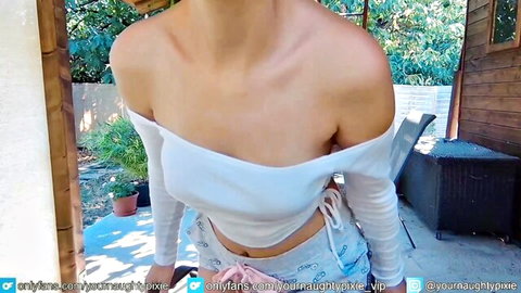 Sexy blonde webcam girl teasing deep cleavage in off-shoulder white crop top and shorts outdoors