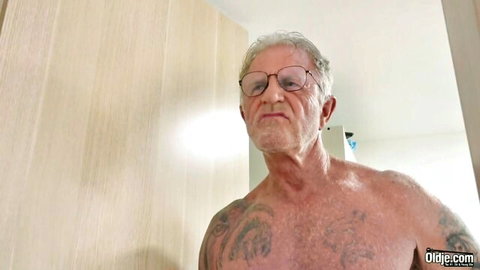 Shirtless older tattooed man in glasses, prepping for hardcore pounding of slim young chick