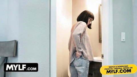 Mature cougar in sweater and ripped jeans gazing in bathroom mirror, prepping for stepson fantasy