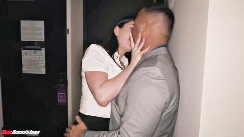 Curvy brunette in tight white top passionately kisses muscular suited boss against hotel door gripping his face