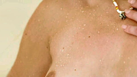 Wet topless woman in steamy shower touching beaded necklace, erotic close-up