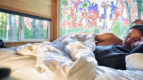 Sensual couple spooning intimately under sheets in cozy sunlit cabin bed