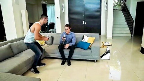 Muscular brunette in tank top leans over skinny fair twink on sofa in living room