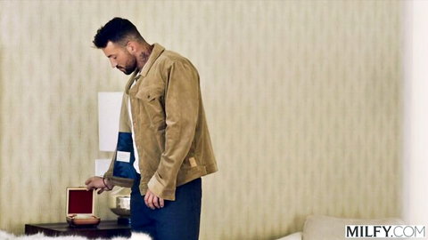 Bearded man in suede jacket examines open ring box in luxury room