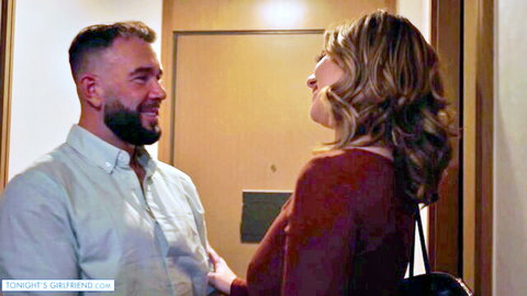 Blonde woman in tight maroon top flirts intimately with bearded man in hallway doorway
