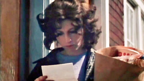 Vintage brunette wife in blue shirt holding letter and bag at door, classic Golden Age tease