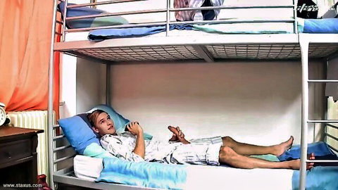 Xander Hollis relaxing on bed in shirt and shorts, teasing gay anal session