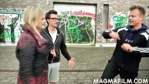 Surprised blonde woman in coat with two guys gesturing playfully on graffiti street