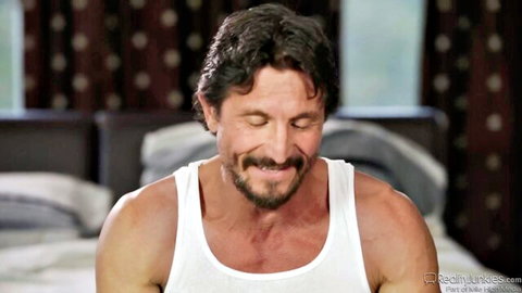 Handsome muscular DILF stepdad smiling in tight white tank top on bed